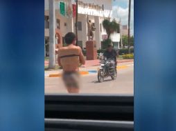 El joven, con los brazos atados y ocultándose el rostro, el cual solo llevaba puestos 