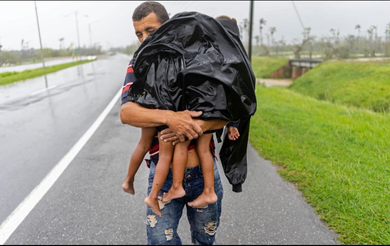 Un hombre carga a sus dos hijos, bajo la lluvia, luego de que el huracán 