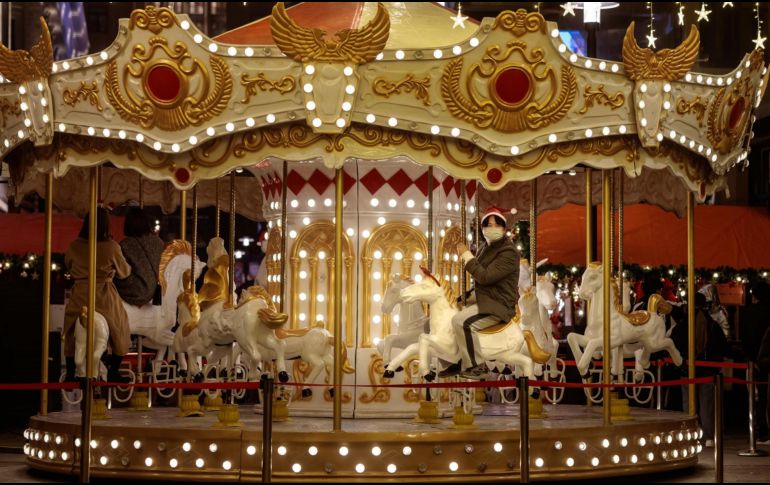 Un hombre con cubrebocas monta en un carrusel en la víspera del día de Navidad. Shanghái, China, recomienda sus ciudadanos que no salgan de sus casas ante la rápida propagación del COVID-19. EFE / A. Plavevski