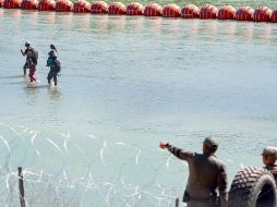 Oficiales fronterizos de Texas vigilan el Río Bravo mientras algunos migrantes caminan junto al muro de boyas. AFP