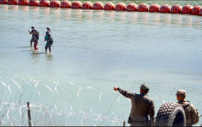 Oficiales fronterizos de Texas vigilan el Río Bravo mientras algunos migrantes caminan junto al muro de boyas. AFP