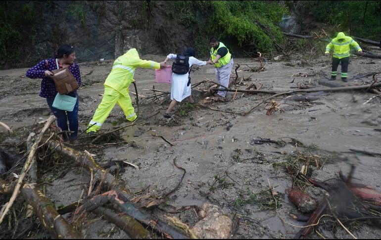 Gente recibe ayuda para cruzar una carretera bloqueada por un deslizamiento de tierra provocado por el huracán 