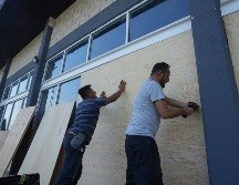 Empleados de una tienda de muebles cubren las ventanas con tablones ante de la llegada del huracán 