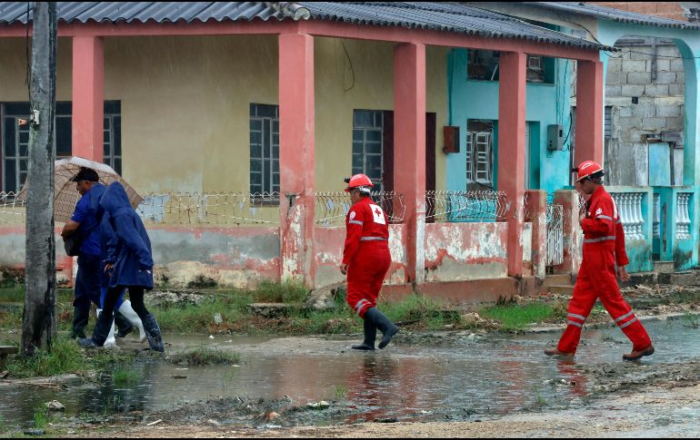 Integrantes de la Cruz Roja cubana caminan junto a unas personas durante una evacuación ante la llegada del huracán Rafael, este miércoles en Surgidero de Batabanó, un puerto pesquero en la provincia occidental de Mayabeque, a unos 50 kilómetros al sur de La Habana (Cuba). EFE/ E. Mastrascusa.