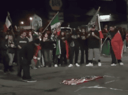 Las imágenes muestran a un grupo de manifestantes colocando la bandera en el suelo y prendiéndole fuego mientras varios de ellos gritan y ondean banderas mexicanas. ESPECIAL.