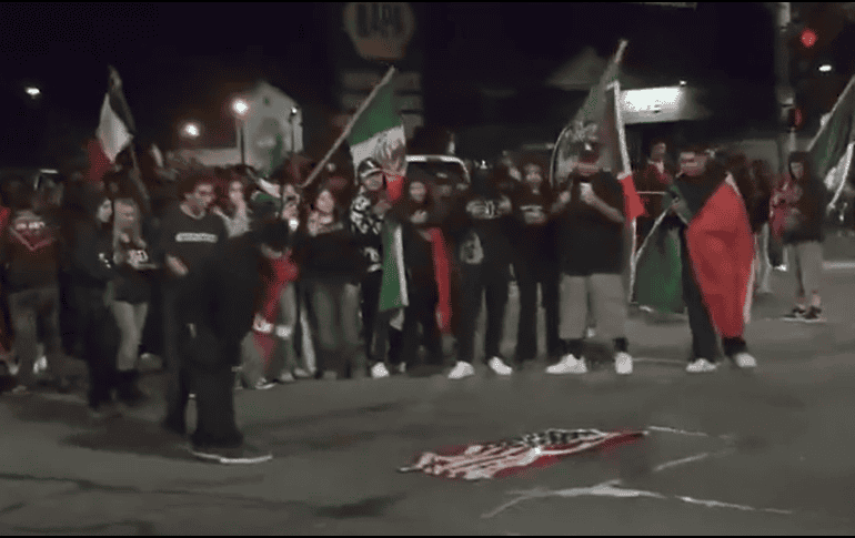 Las imágenes muestran a un grupo de manifestantes colocando la bandera en el suelo y prendiéndole fuego mientras varios de ellos gritan y ondean banderas mexicanas. ESPECIAL.