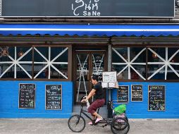 Una mujer en triciclo pasa junto a un restaurante con las ventanas selladas con una X como medida de precaución ante la proximidad del tifón Ragasa en Hong Kong. EFE/M. James