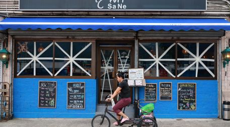Una mujer en triciclo pasa junto a un restaurante con las ventanas selladas con una X como medida de precaución ante la proximidad del tifón Ragasa en Hong Kong. EFE/M. James