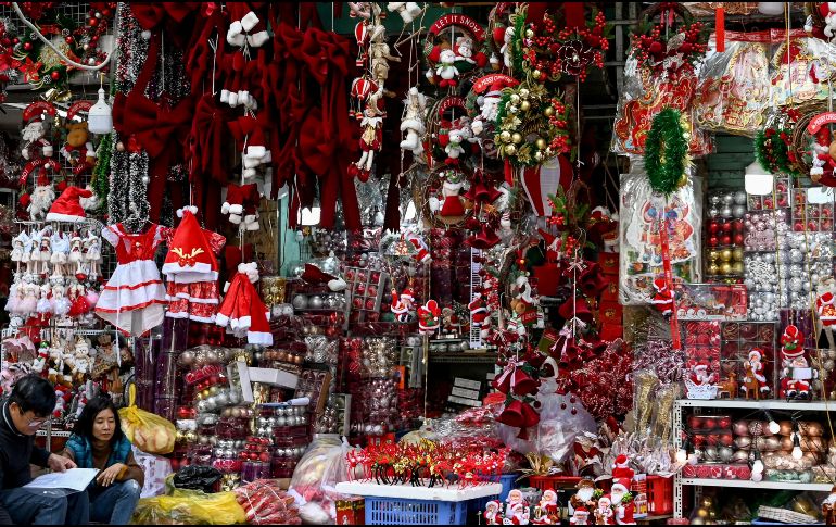 Vendedores sentados frente a su tienda vendiendo adornos navideños en Hanói, Vietnam. AFP / Nhac Nguyen