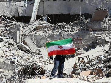 Un iraní coloca la bandera nacional de Irán entre las ruinas de una comisaría de policía dañada en el centro de Teherán, Irán, este miércoles. EFE/ A. Taherkenareh